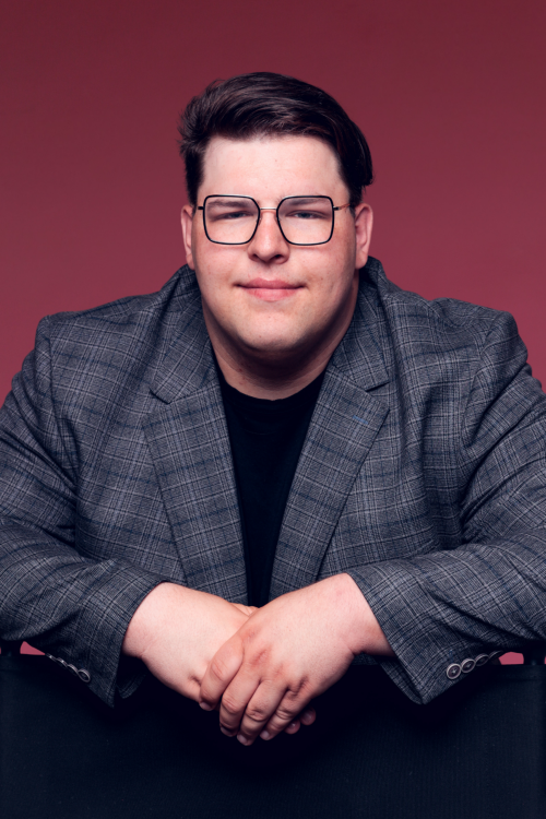 Portraitaufnahme von Lars Leuverink im schwarzen Shirt und grauem Sakko vor einem roten Hintergrund